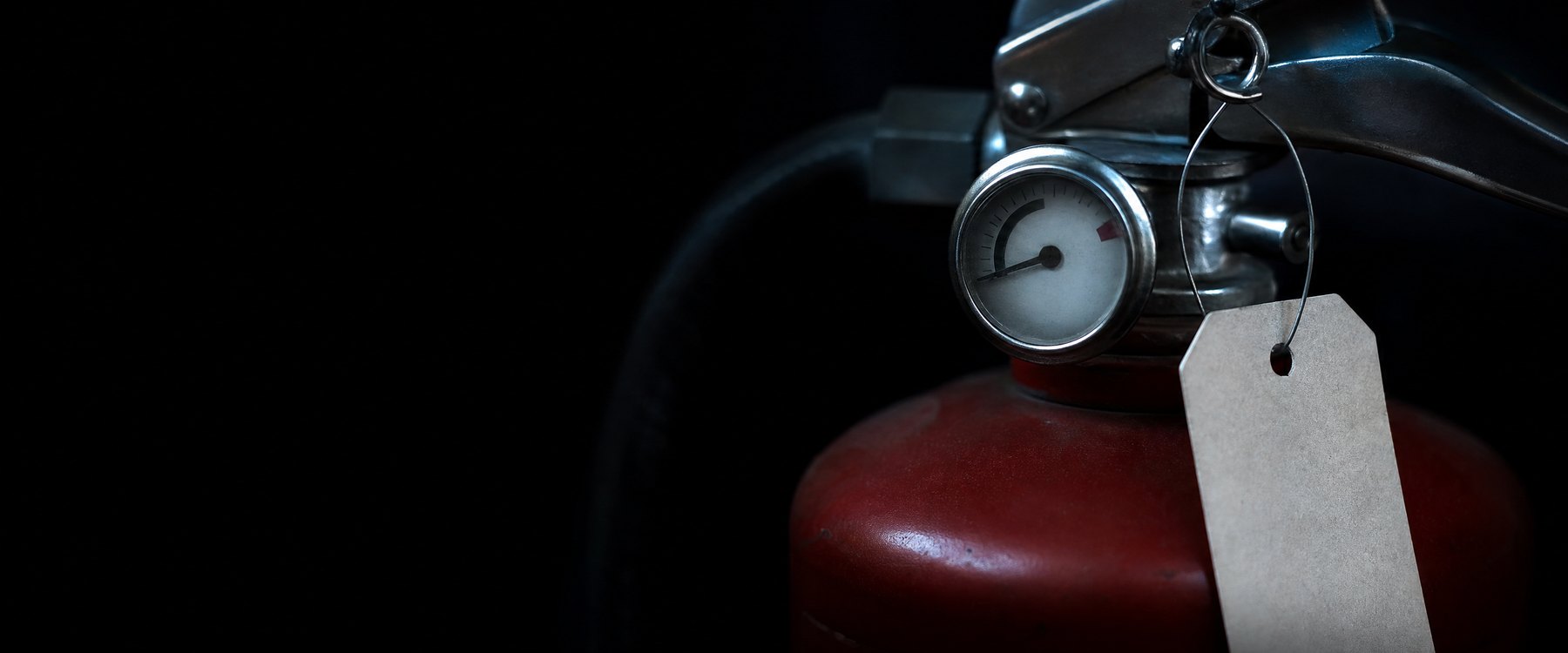 Nahaufnahme des Ventils eines Feuerlöschers mit unbeschriftetem Prüfanhänger (Symbolbild)