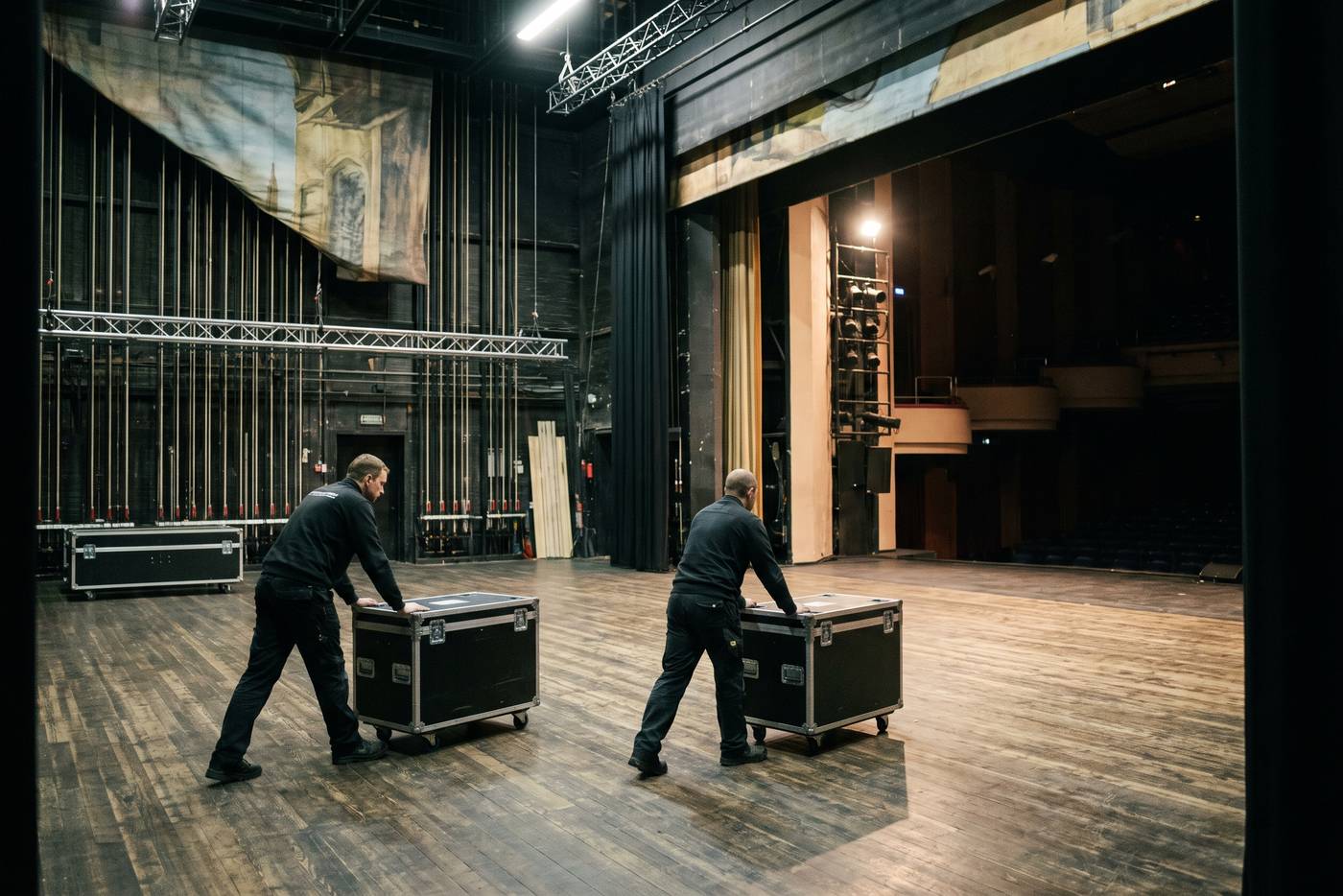 Zwei Techniker schieben Flightcases über die Bühne eines Theaters während eines Umbaus (Symbolbild)